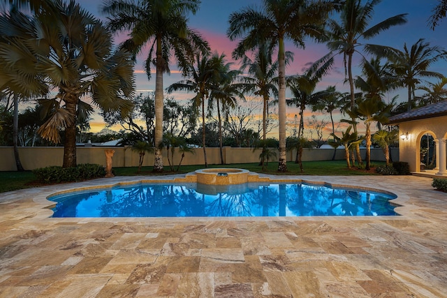 pool at dusk featuring a patio and an in ground hot tub