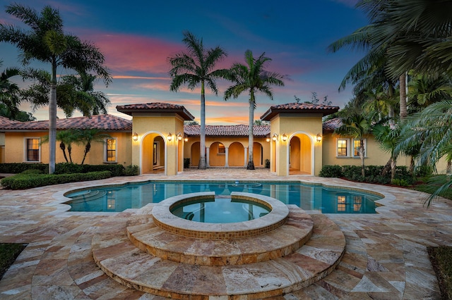 pool at dusk with an in ground hot tub and a patio