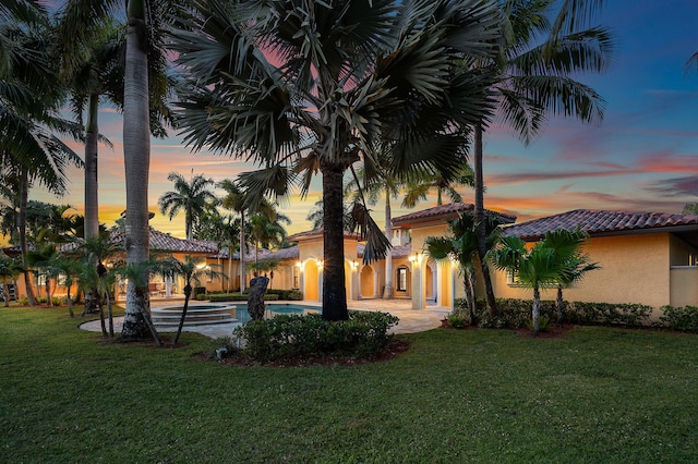 back house at dusk featuring a patio area and a lawn