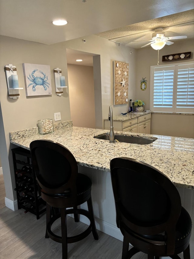 kitchen with light stone countertops, kitchen peninsula, a breakfast bar, sink, and light hardwood / wood-style floors