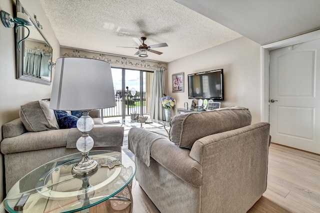 living room featuring ceiling fan, light hardwood / wood-style flooring, and a textured ceiling