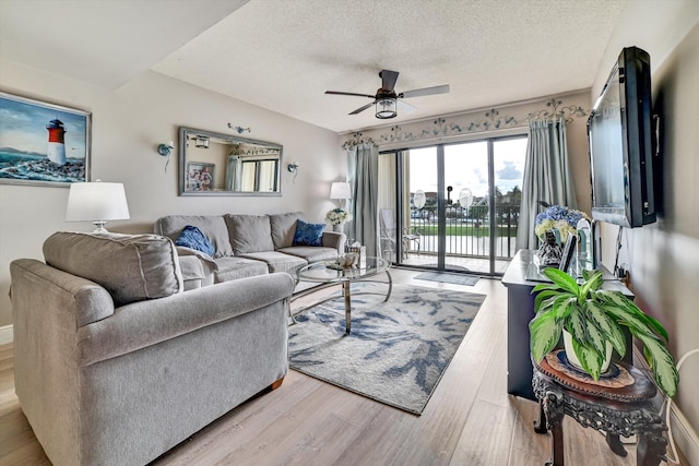 living room with ceiling fan, a textured ceiling, and light hardwood / wood-style flooring