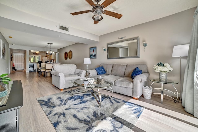 living room with ceiling fan with notable chandelier and light hardwood / wood-style floors