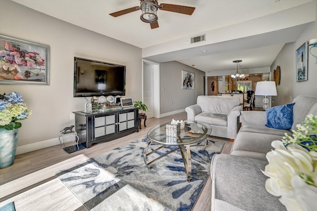 living room with ceiling fan with notable chandelier and light hardwood / wood-style floors