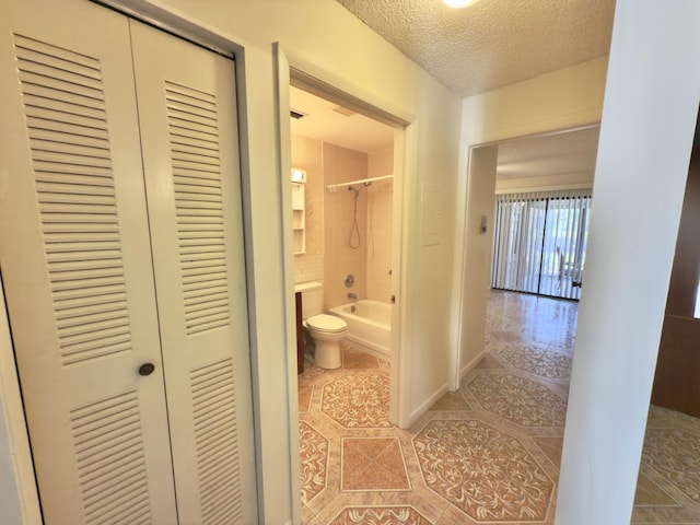 bathroom featuring a textured ceiling, toilet, and tiled shower / bath