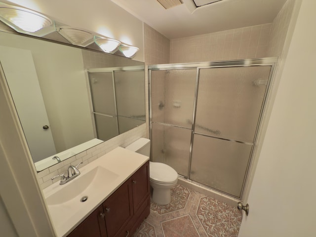 bathroom featuring vanity, toilet, a shower with door, and tasteful backsplash