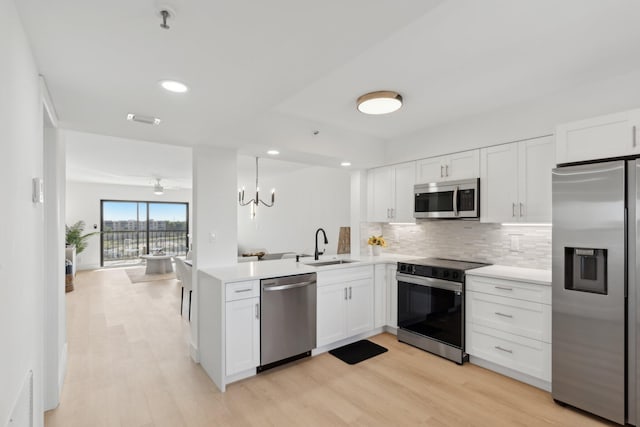 kitchen featuring sink, kitchen peninsula, appliances with stainless steel finishes, decorative light fixtures, and white cabinetry