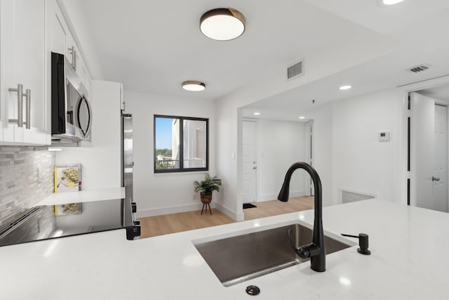 kitchen featuring decorative backsplash, stainless steel appliances, sink, light hardwood / wood-style flooring, and white cabinetry