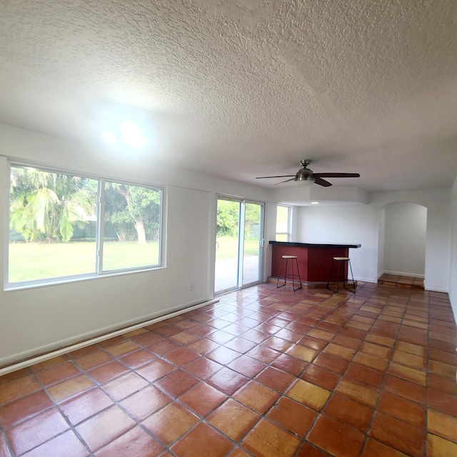 unfurnished living room with a textured ceiling, ceiling fan, and dark tile patterned flooring