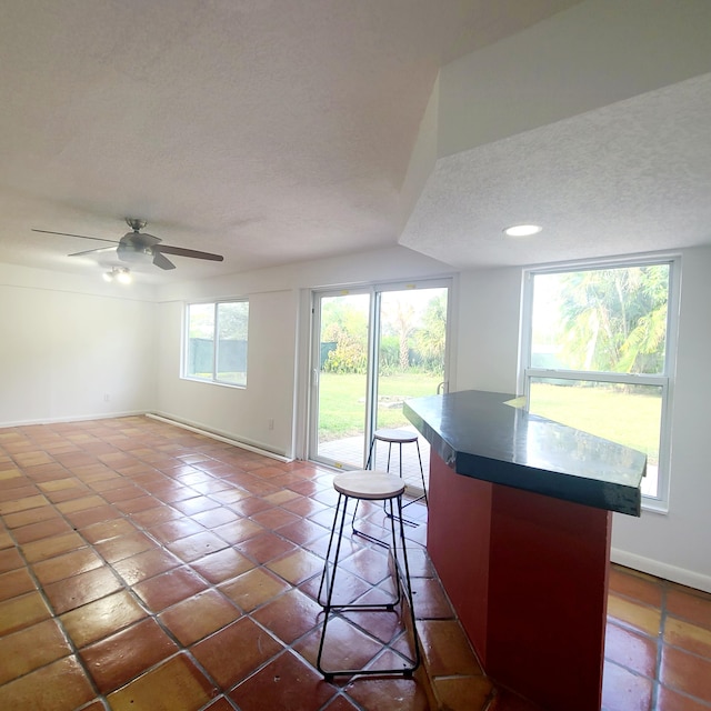 kitchen featuring a textured ceiling, a kitchen bar, ceiling fan, and a healthy amount of sunlight