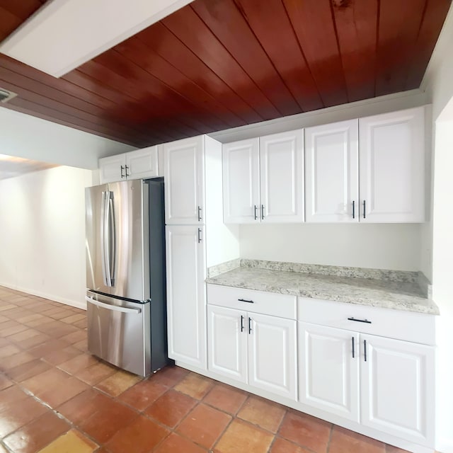 kitchen with light stone countertops, white cabinets, wood ceiling, and stainless steel fridge