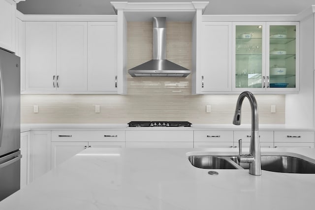 kitchen with black gas cooktop, white cabinets, wall chimney exhaust hood, stainless steel fridge, and tasteful backsplash