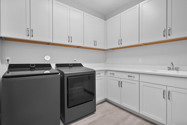 laundry room featuring cabinet space, a sink, light wood-style flooring, and washing machine and clothes dryer