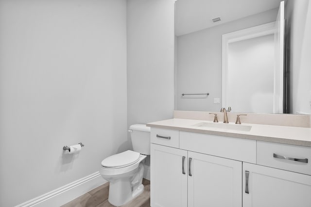 half bath with visible vents, toilet, vanity, wood finished floors, and baseboards