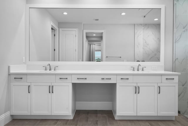 bathroom featuring double vanity, wood finish floors, a sink, and recessed lighting