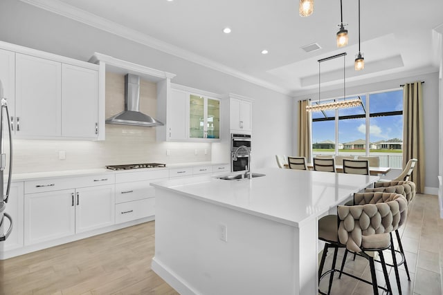 kitchen featuring gas cooktop, a sink, wall chimney range hood, a raised ceiling, and crown molding