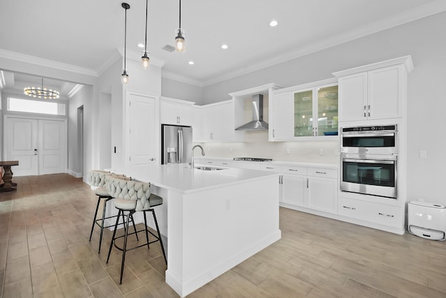 kitchen with appliances with stainless steel finishes, light countertops, wall chimney range hood, a kitchen bar, and a sink