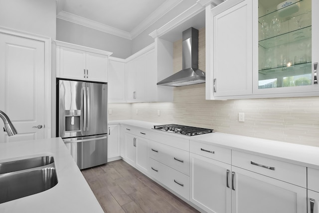 kitchen featuring stainless steel appliances, a sink, ornamental molding, wall chimney range hood, and tasteful backsplash