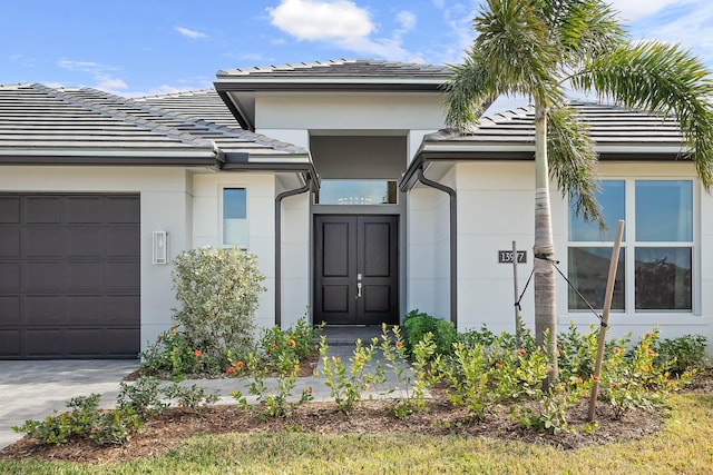 doorway to property with driveway, a tiled roof, an attached garage, and stucco siding