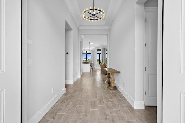 corridor featuring crown molding, wood finish floors, baseboards, and a notable chandelier