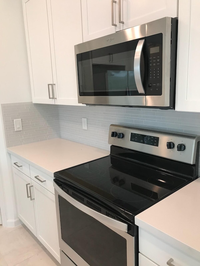 kitchen featuring backsplash, white cabinets, light tile patterned floors, and appliances with stainless steel finishes