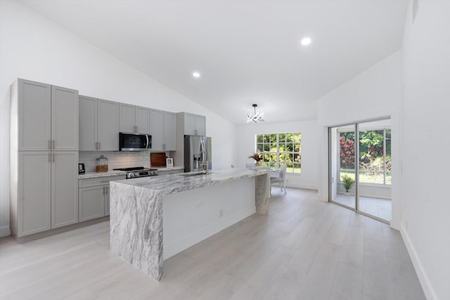 kitchen with stainless steel appliances, light stone counters, gray cabinets, decorative backsplash, and a center island with sink