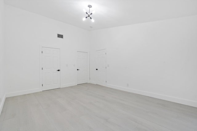 empty room with light hardwood / wood-style flooring, a high ceiling, and a chandelier