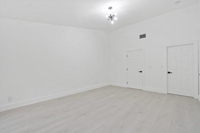 spare room featuring a chandelier and light hardwood / wood-style flooring