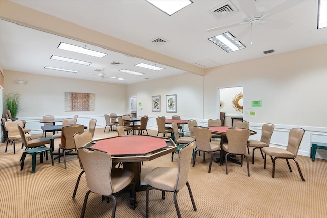 carpeted dining area with ceiling fan and beamed ceiling