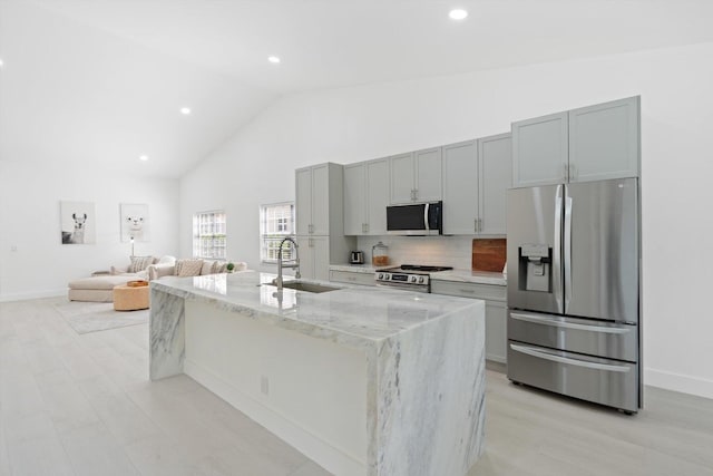 kitchen featuring light stone countertops, appliances with stainless steel finishes, tasteful backsplash, sink, and a center island with sink