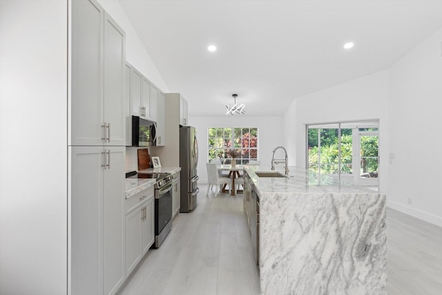 kitchen with a center island with sink, sink, light stone countertops, light hardwood / wood-style floors, and stainless steel appliances