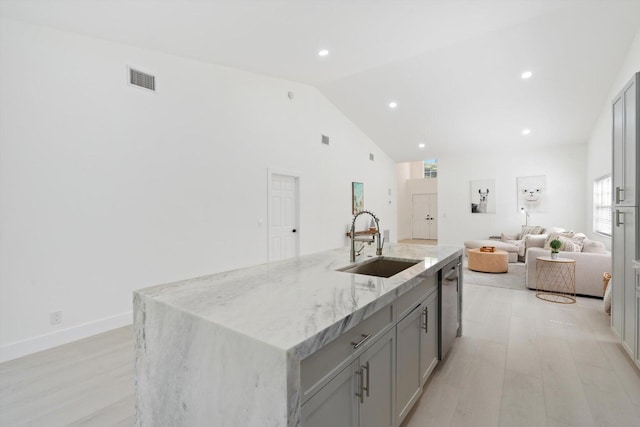 kitchen with gray cabinetry, light stone countertops, sink, dishwasher, and a kitchen island with sink