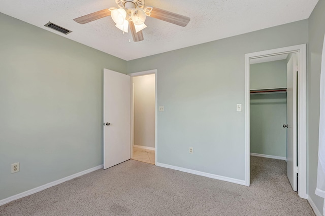 unfurnished bedroom with a spacious closet, ceiling fan, light carpet, a textured ceiling, and a closet