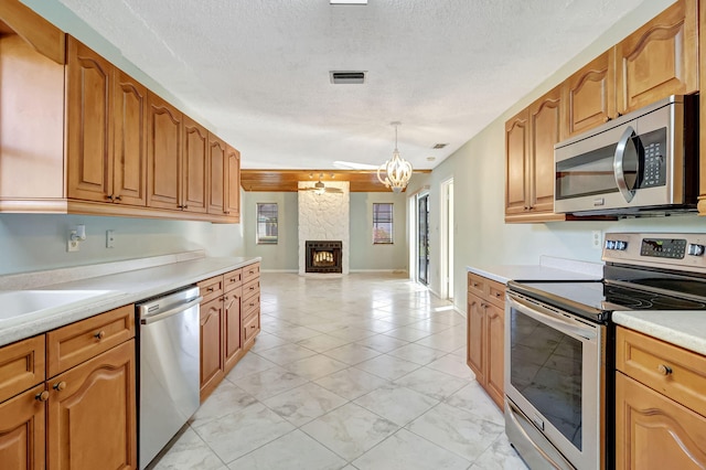 kitchen featuring hanging light fixtures, a textured ceiling, a notable chandelier, stainless steel appliances, and a fireplace