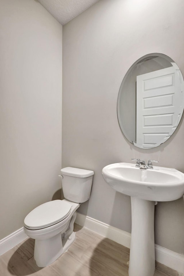 bathroom with a textured ceiling, toilet, wood-type flooring, and sink