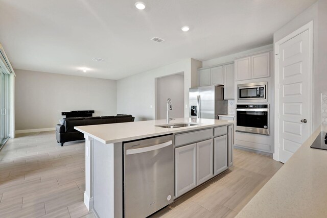 kitchen with gray cabinetry, a kitchen island with sink, sink, and stainless steel appliances