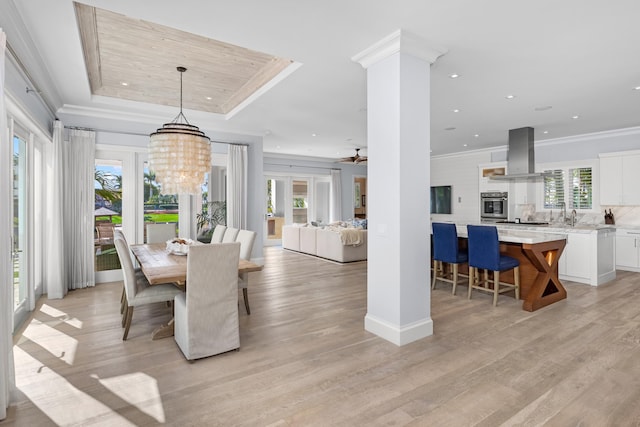 dining area with a tray ceiling, light hardwood / wood-style floors, ceiling fan with notable chandelier, and ornamental molding