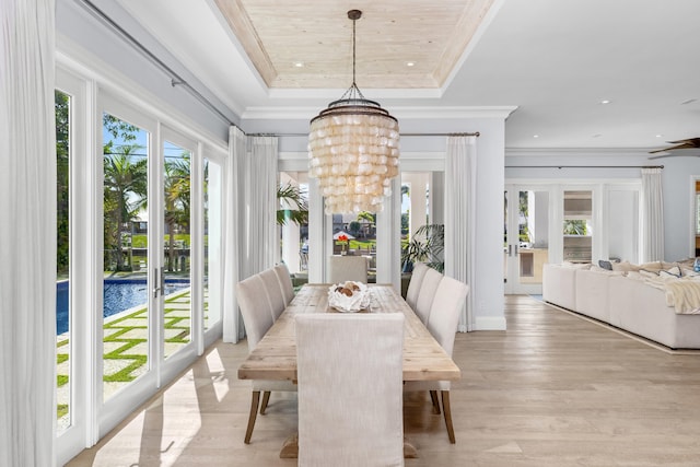 dining space with french doors, light wood-type flooring, a tray ceiling, crown molding, and a notable chandelier