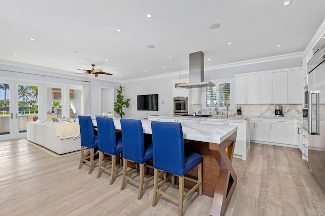 kitchen featuring stainless steel oven, island range hood, a spacious island, light hardwood / wood-style flooring, and white cabinetry