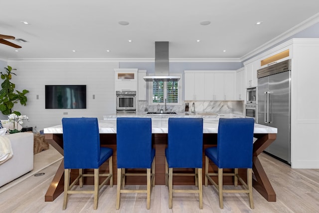 kitchen with a kitchen breakfast bar, built in appliances, island range hood, and white cabinetry