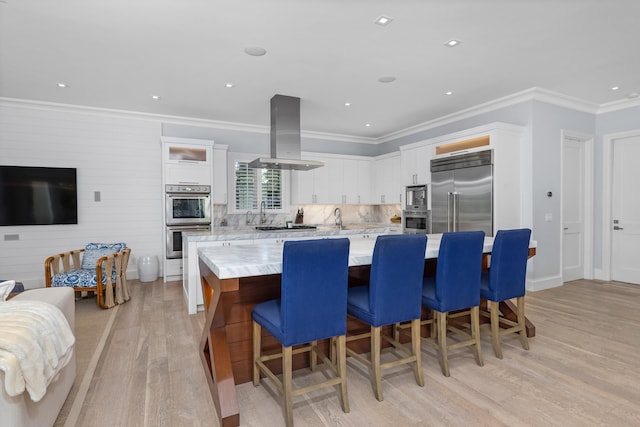 kitchen featuring built in appliances, a large island, island range hood, white cabinetry, and a breakfast bar area