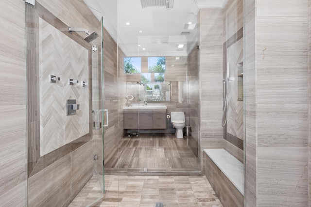 bathroom with vanity, toilet, a shower with door, and tile walls