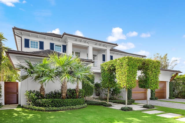 view of front of property featuring a balcony, driveway, a front yard, and stucco siding