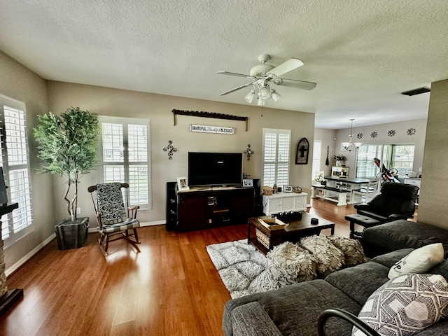 living room with hardwood / wood-style flooring, ceiling fan with notable chandelier, and a textured ceiling