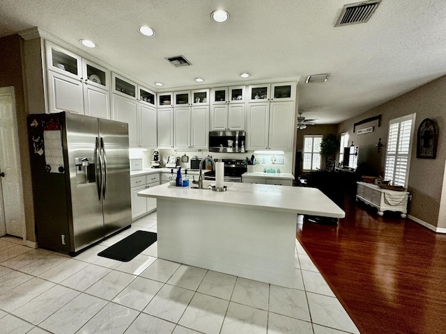 kitchen featuring white cabinets, ceiling fan, an island with sink, appliances with stainless steel finishes, and light tile patterned flooring