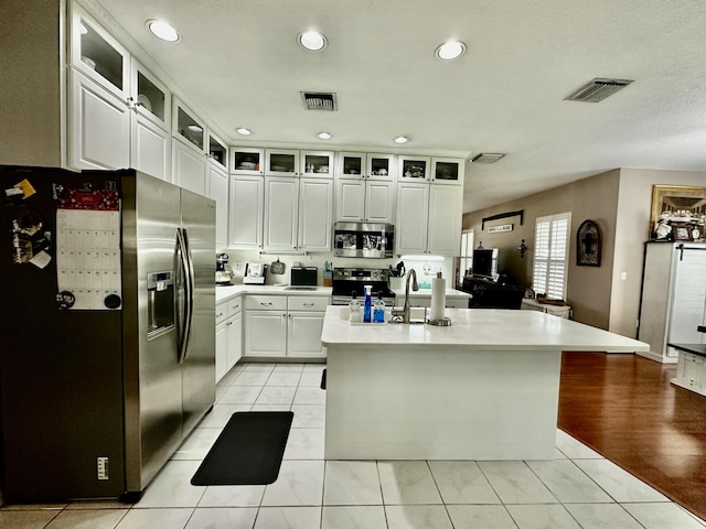 kitchen with a kitchen island with sink, sink, appliances with stainless steel finishes, light tile patterned flooring, and white cabinetry