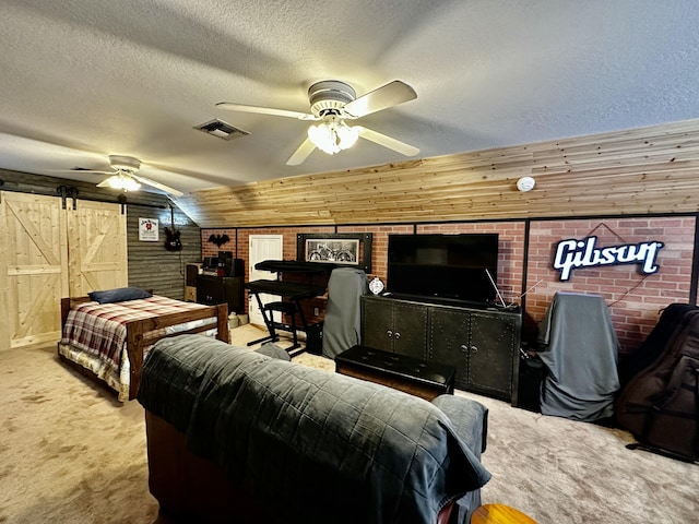 bedroom featuring carpet, wood walls, ceiling fan, a barn door, and a textured ceiling