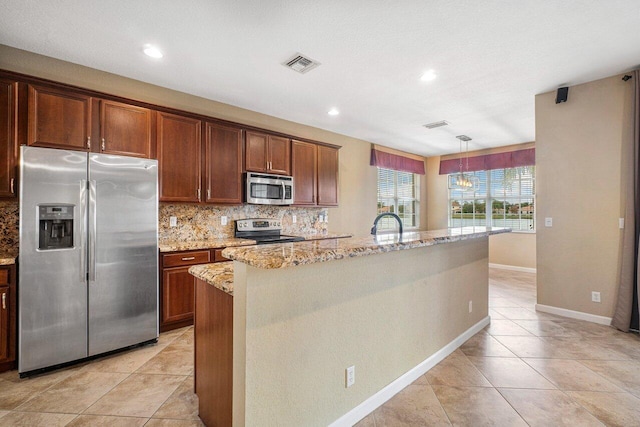 kitchen with backsplash, an inviting chandelier, a center island with sink, appliances with stainless steel finishes, and light stone counters