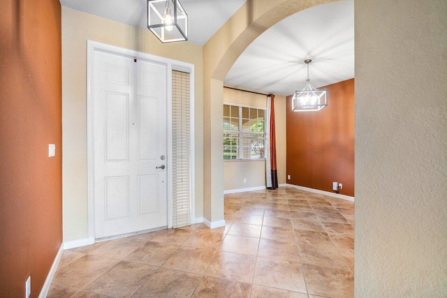 foyer entrance with arched walkways, light tile patterned flooring, a notable chandelier, and baseboards