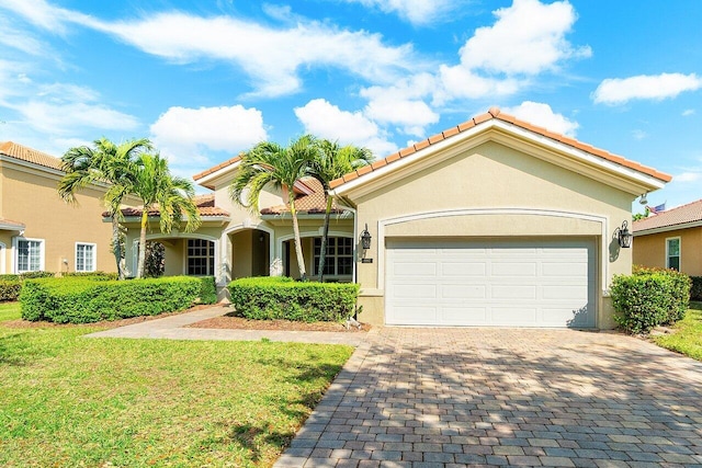 mediterranean / spanish-style house featuring decorative driveway, stucco siding, an attached garage, a tiled roof, and a front lawn